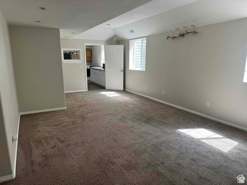 Unfurnished living room with carpet floors, lofted ceiling, baseboards, and a sink