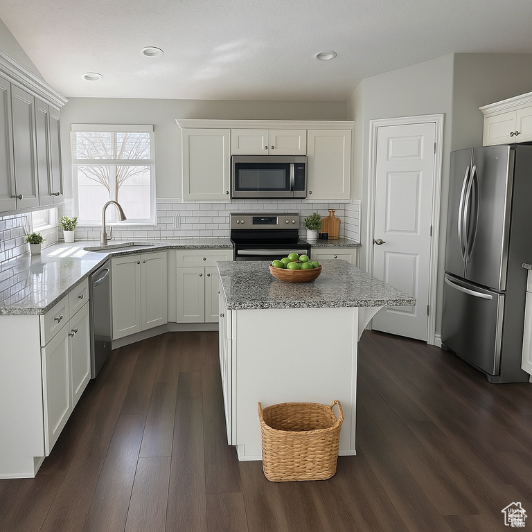 Kitchen featuring stainless steel appliances, a sink, white cabinets, light stone countertops, and decorative backsplash