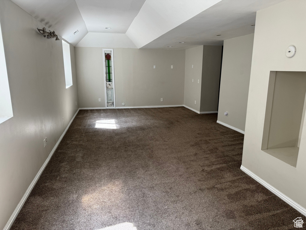 Empty room with dark colored carpet, baseboards, and lofted ceiling