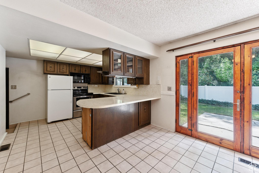 Kitchen with freestanding refrigerator, stainless steel range with electric stovetop, black microwave, a peninsula, and light countertops