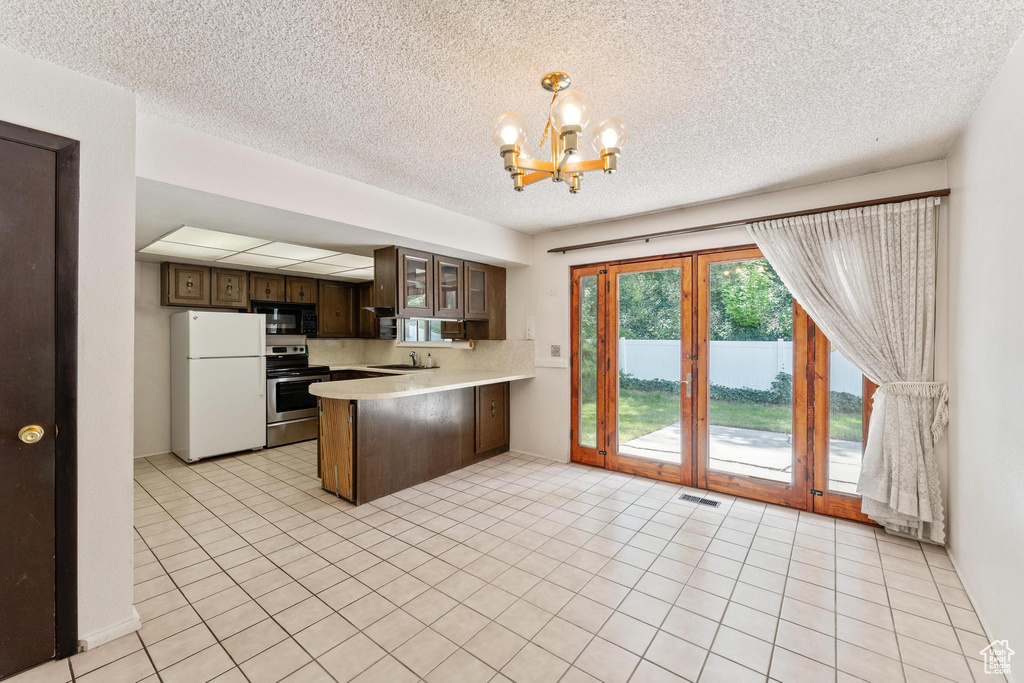 Kitchen featuring black microwave, freestanding refrigerator, electric range, a chandelier, and light countertops