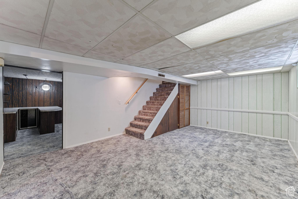 Finished below grade area with carpet floors, stairs, a paneled ceiling, wooden walls, and baseboards