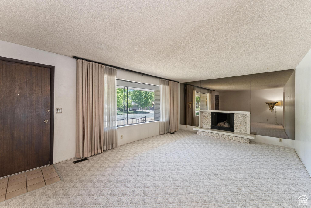 Unfurnished living room with carpet floors, a fireplace with raised hearth, and a textured ceiling