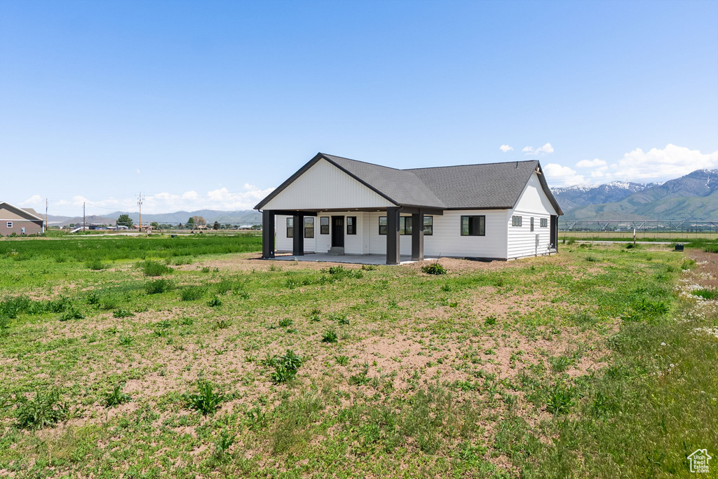 Modern inspired farmhouse featuring a mountain view, a patio, a view of countryside, and a shingled roof