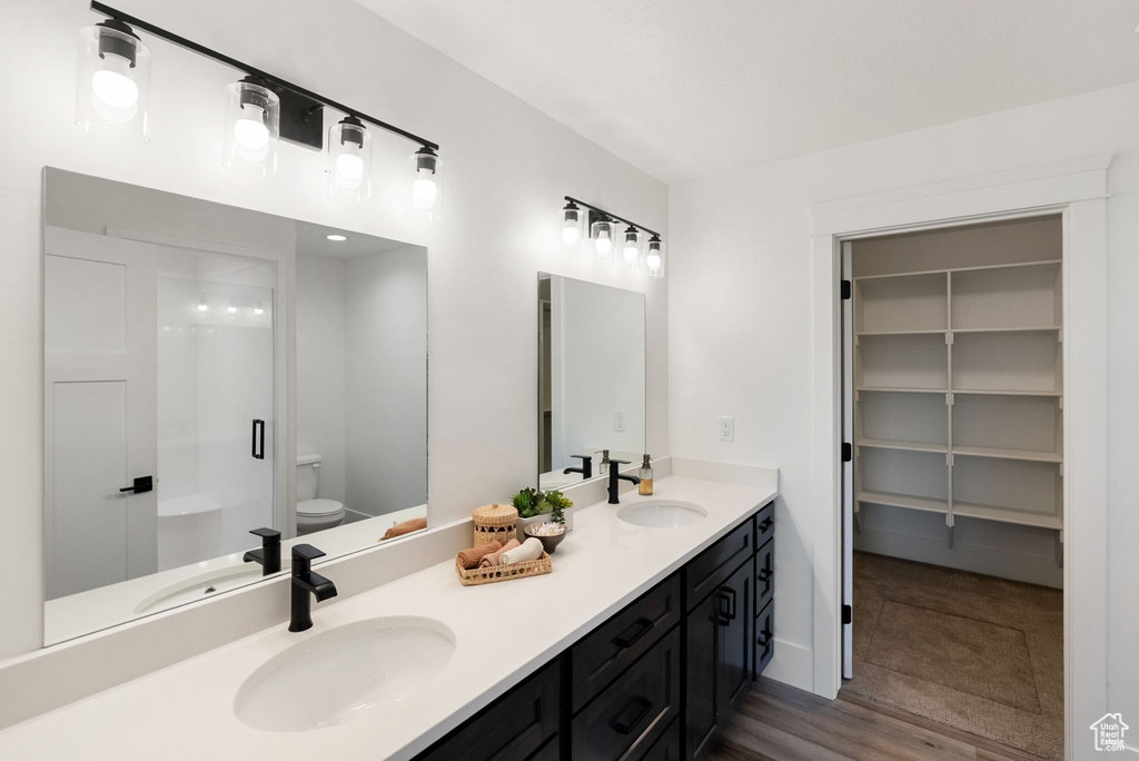 Bathroom featuring double vanity, toilet, a shower with shower door, and wood finished floors
