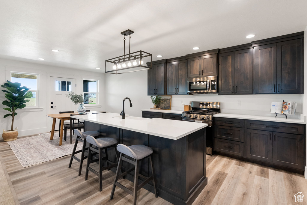 Kitchen featuring stainless steel appliances, light wood finished floors, a kitchen bar, light countertops, and recessed lighting