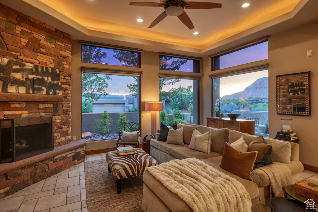 Living room featuring a raised ceiling, a ceiling fan, a fireplace, recessed lighting, and healthy amount of natural light