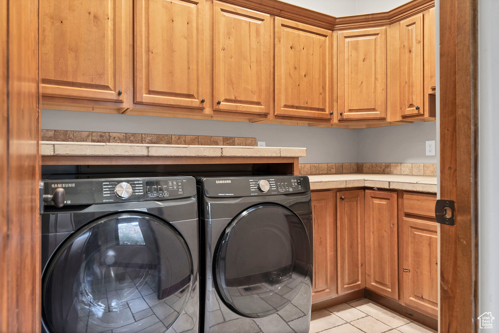 Laundry room with light tile patterned floors, washer and clothes dryer, and cabinet space