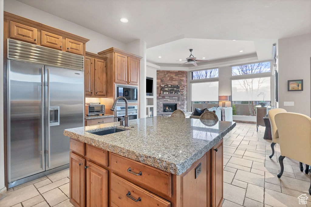 Kitchen with built in appliances, recessed lighting, a fireplace, a sink, and an island with sink