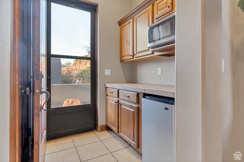 Kitchen with light tile patterned floors, stainless steel microwave, and refrigerator
