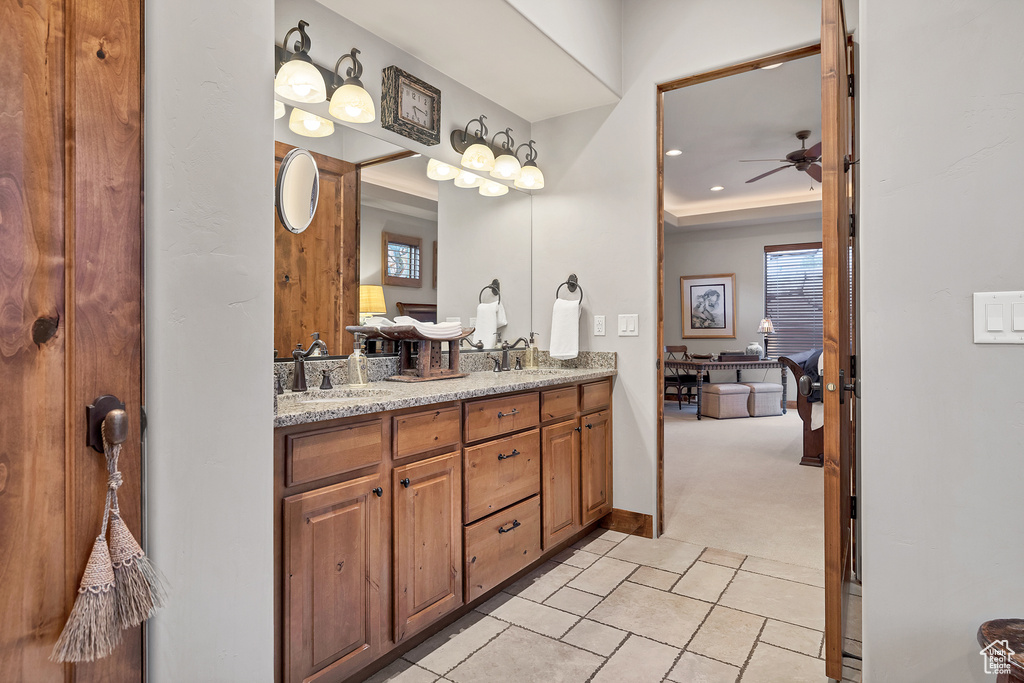 Full bath with a ceiling fan, a tray ceiling, a sink, and double vanity