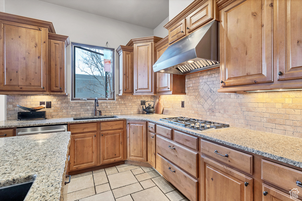 Kitchen featuring light stone counters, stainless steel appliances, decorative backsplash, a sink, and under cabinet range hood
