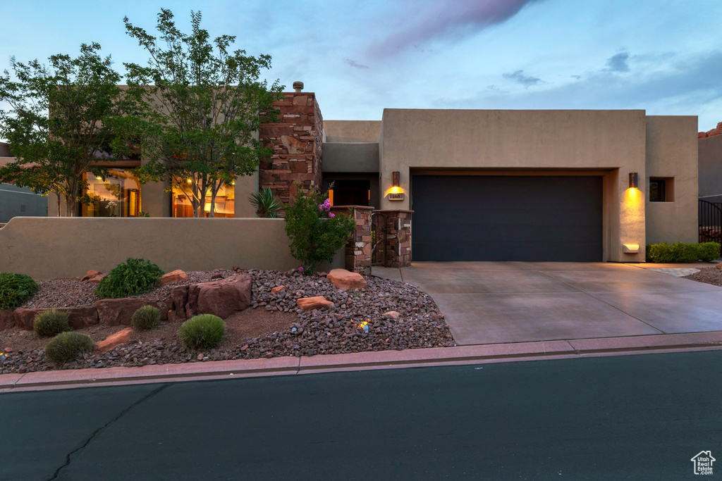 Pueblo-style home with a fenced front yard, an attached garage, concrete driveway, and stucco siding