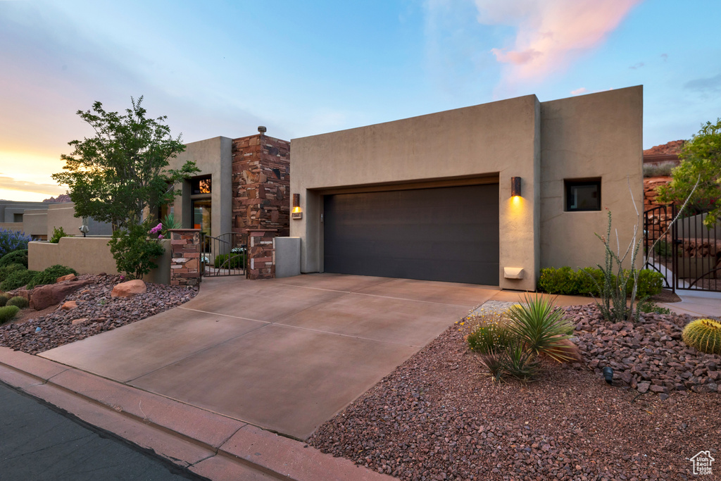 Pueblo-style house with a gate, stucco siding, an attached garage, and concrete driveway