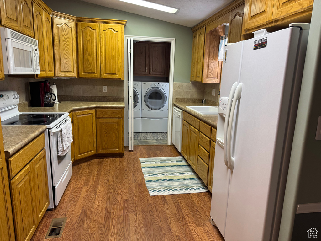 Kitchen featuring white appliances, washer and clothes dryer, dark wood-style flooring, vaulted ceiling, and tasteful backsplash