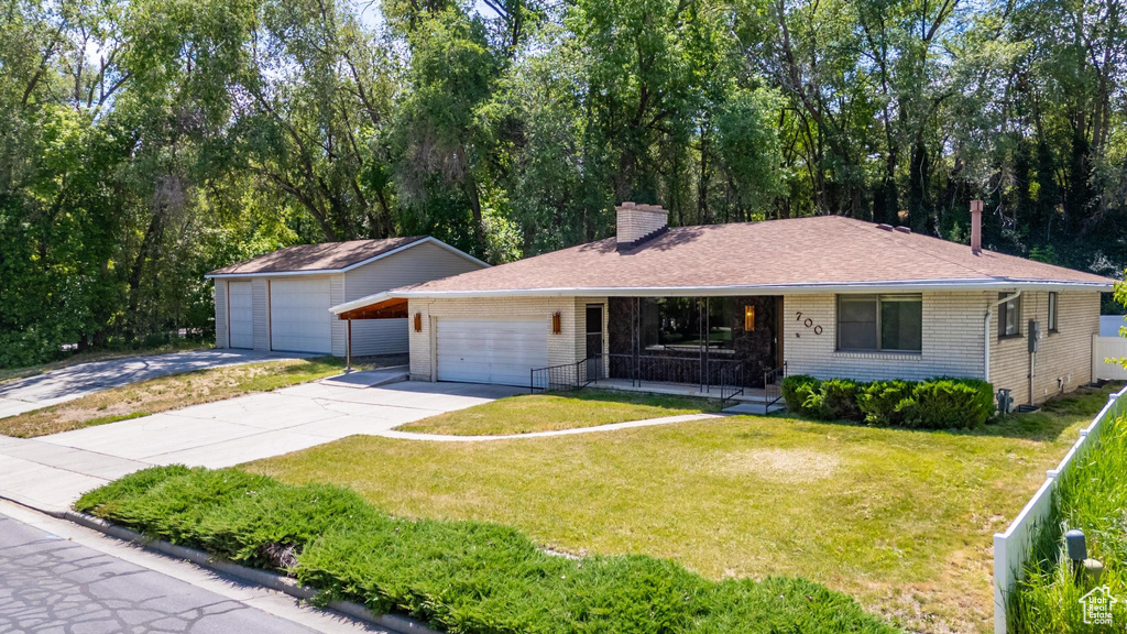 Ranch-style home with concrete driveway, a porch, brick siding, a chimney, and a front lawn