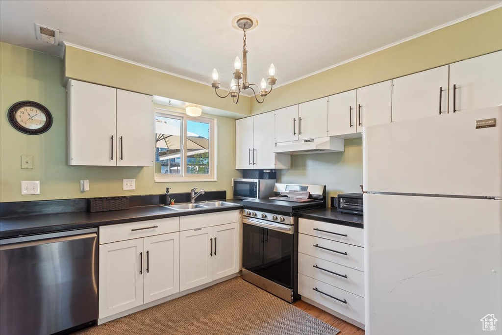 Kitchen with appliances with stainless steel finishes, a sink, under cabinet range hood, dark countertops, and white cabinets