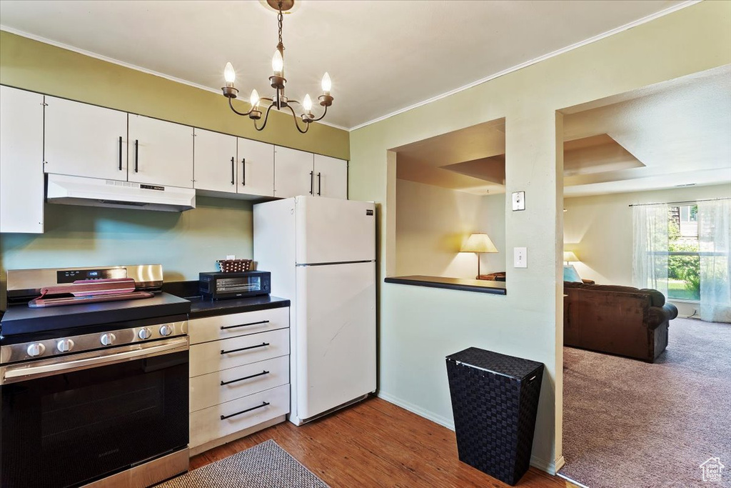 Kitchen with electric range, under cabinet range hood, freestanding refrigerator, a chandelier, and ornamental molding