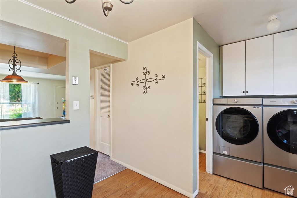 Laundry area featuring separate washer and dryer, cabinet space, light wood-style flooring, and baseboards