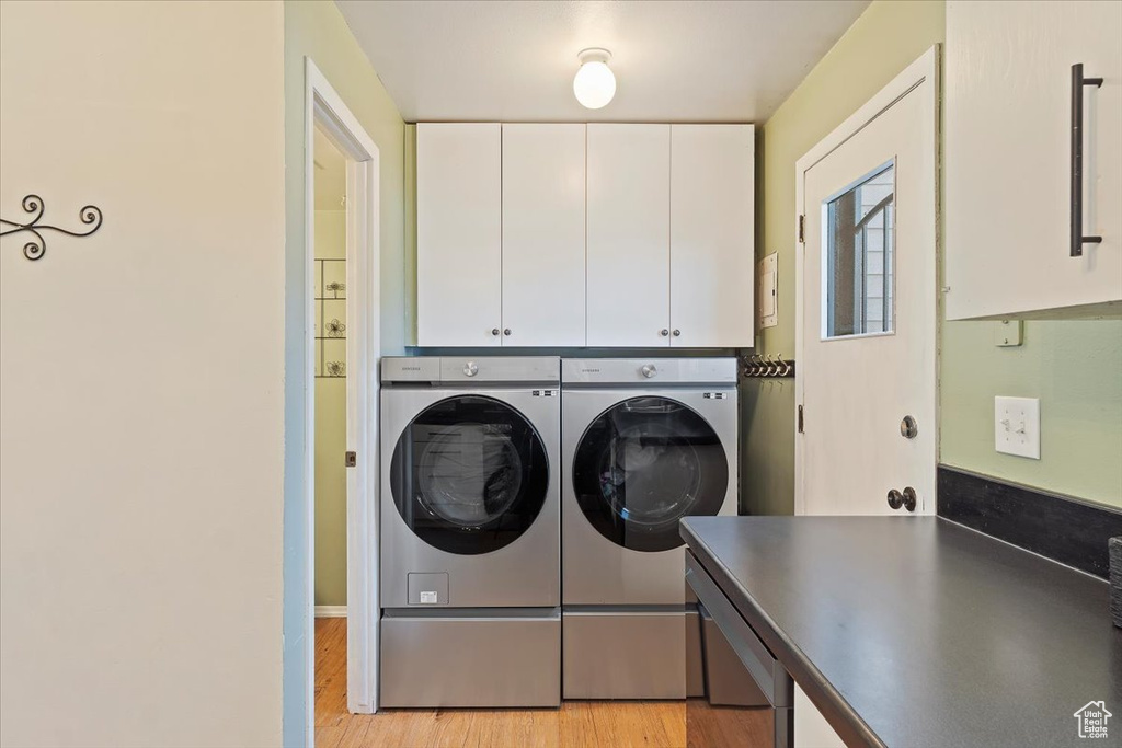 Laundry area with cabinet space, independent washer and dryer, and light wood-style floors