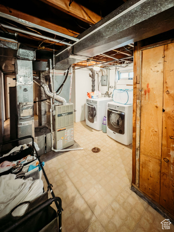 Below grade area with washing machine and clothes dryer, tile patterned floors, heating unit, and electric panel