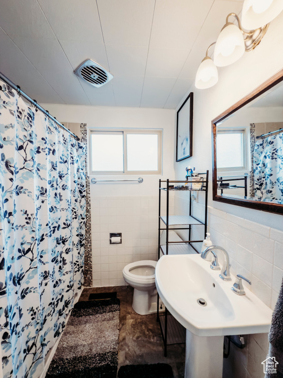 Bathroom featuring tile walls, toilet, and curtained shower