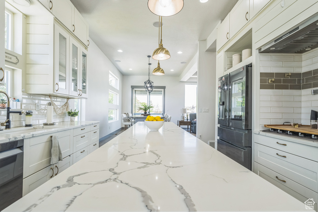 Kitchen with tasteful backsplash, range hood, recessed lighting, refrigerator with ice dispenser, and glass insert cabinets