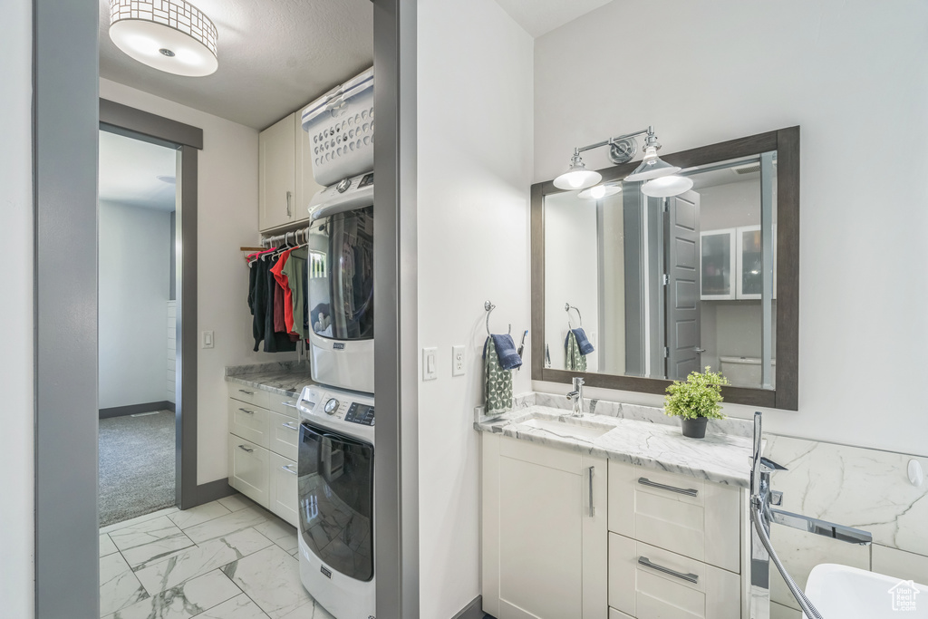 Bathroom featuring estacked washer and dryer, marble finish flooring, vanity, and baseboards