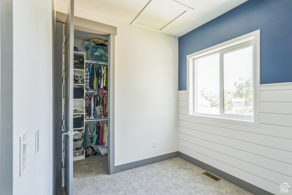 Unfurnished bedroom featuring a closet, a walk in closet, wood walls, attic access, and carpet flooring