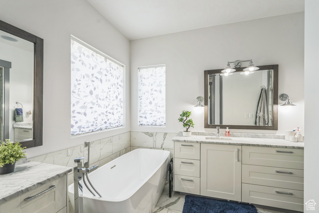 Full bathroom featuring a freestanding bath, vanity, marble look tile flooring, and tile walls