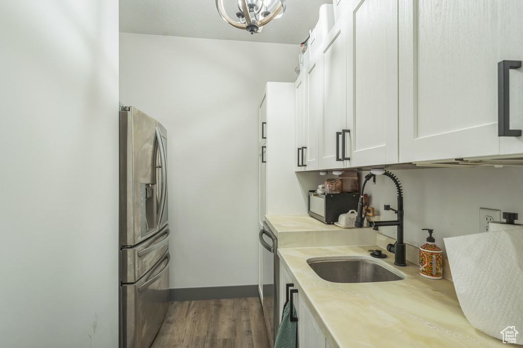Kitchen with appliances with stainless steel finishes, light countertops, a sink, dark wood-style flooring, and white cabinetry