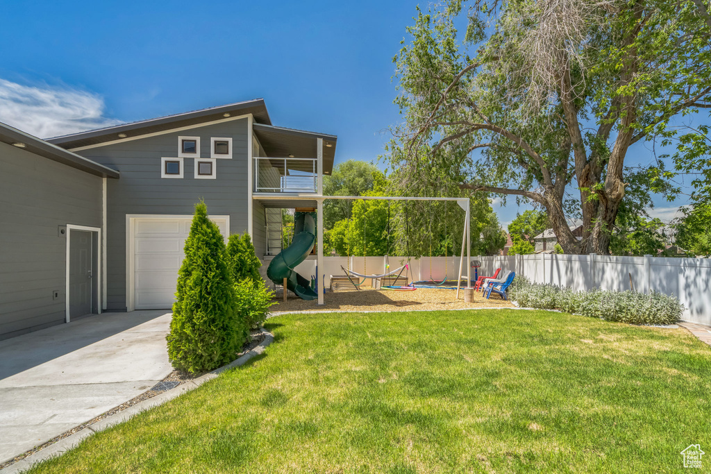 View of yard featuring a playground, driveway, a balcony, and an attached garage