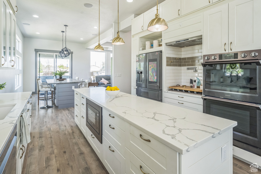 Kitchen featuring double oven, stainless steel fridge, built in microwave, ventilation hood, and wood finished floors