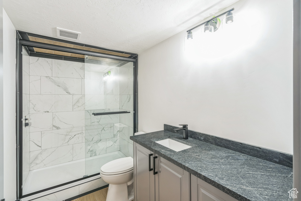 Bathroom with toilet, vanity, a shower stall, wood finished floors, and a textured ceiling