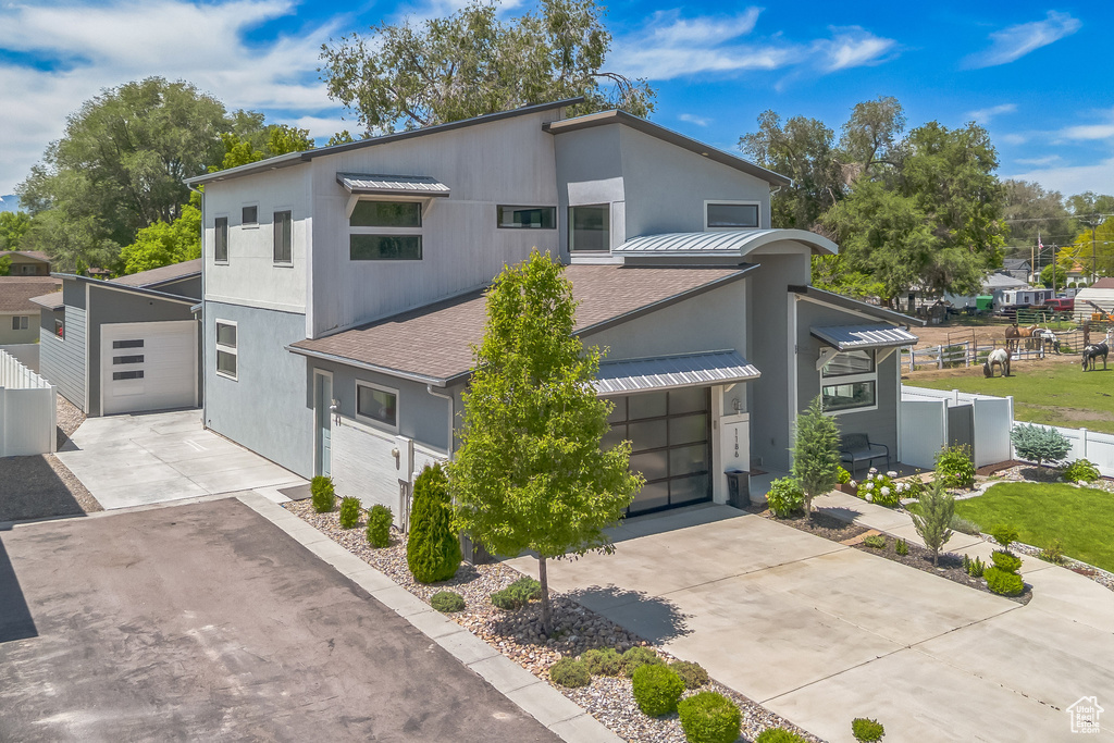 Contemporary house featuring driveway, a shingled roof, stucco siding, and metal roof