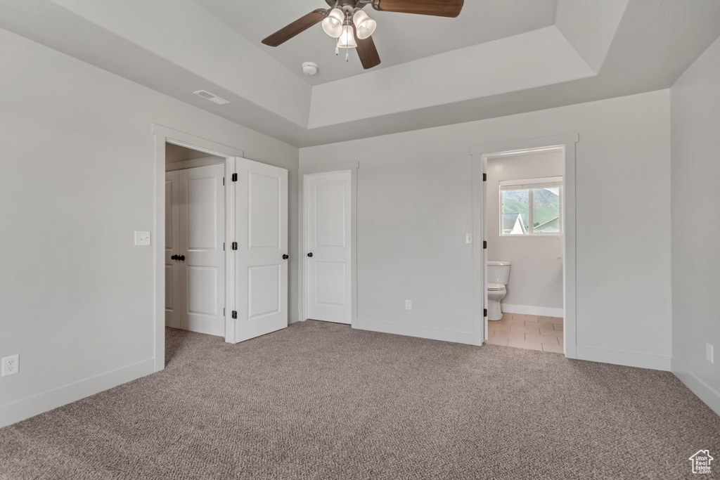 Unfurnished bedroom with light colored carpet, a raised ceiling, baseboards, and ensuite bath