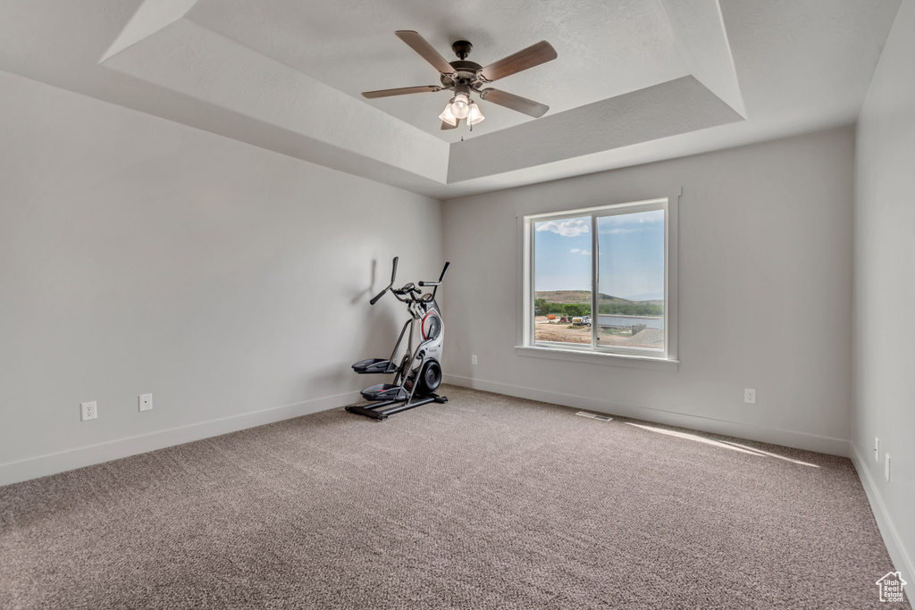 Exercise room featuring a tray ceiling, ceiling fan, baseboards, and carpet