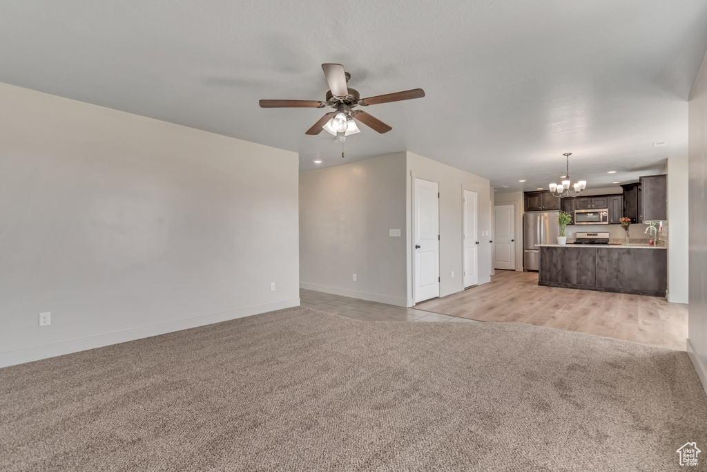 Unfurnished living room with light colored carpet, a chandelier, ceiling fan, baseboards, and recessed lighting