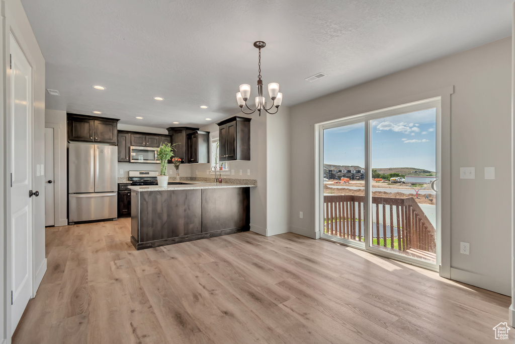 Kitchen with stainless steel appliances, a chandelier, dark brown cabinetry, light wood-style flooring, and a peninsula