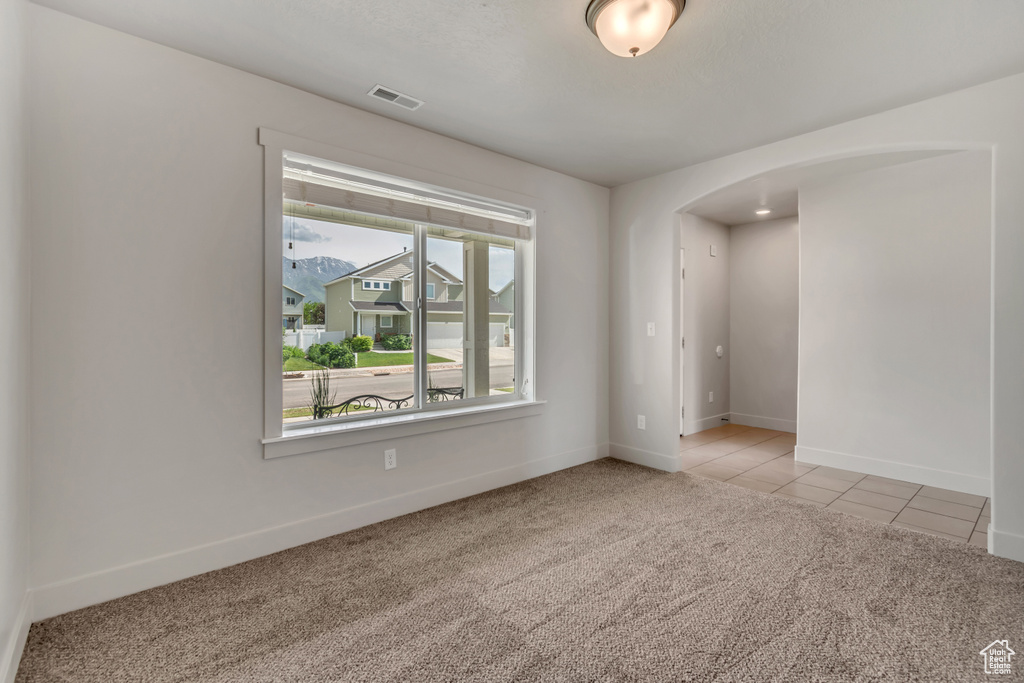 Spare room featuring arched walkways, light colored carpet, baseboards, and light tile patterned floors