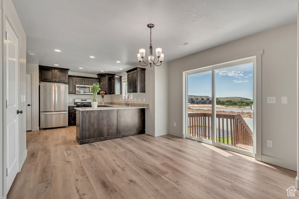 Kitchen featuring appliances with stainless steel finishes, a chandelier, dark brown cabinets, light wood-style flooring, and a peninsula