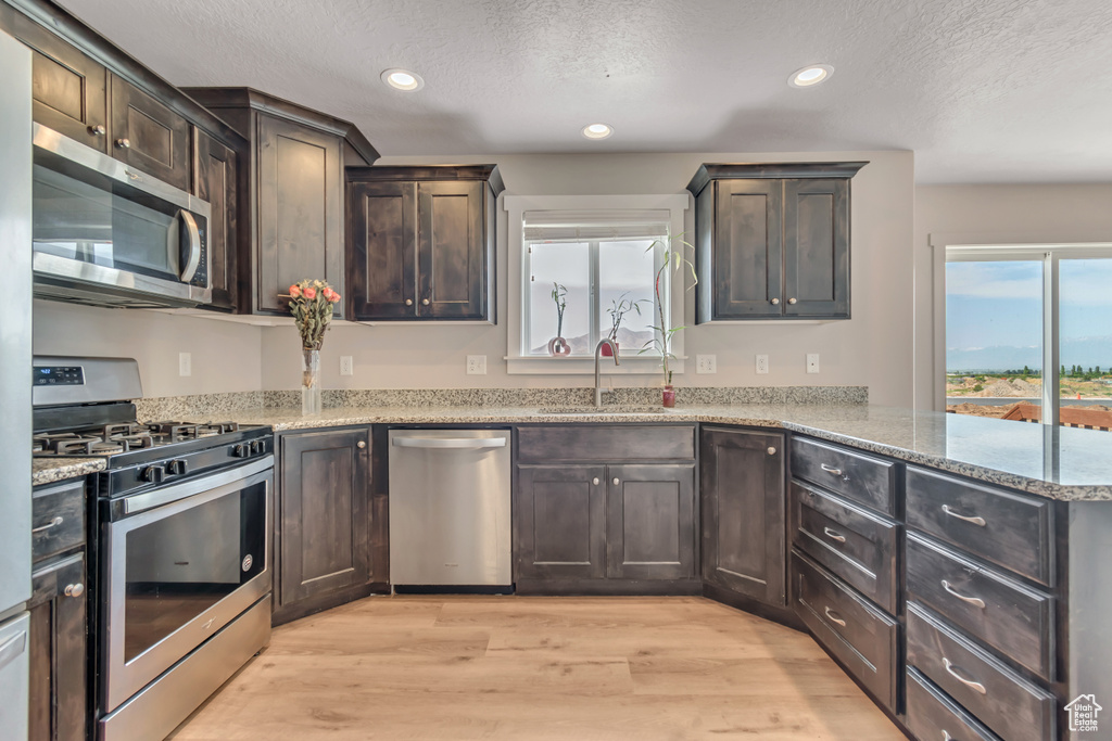 Kitchen featuring appliances with stainless steel finishes, a sink, a textured ceiling, recessed lighting, and light wood finished floors