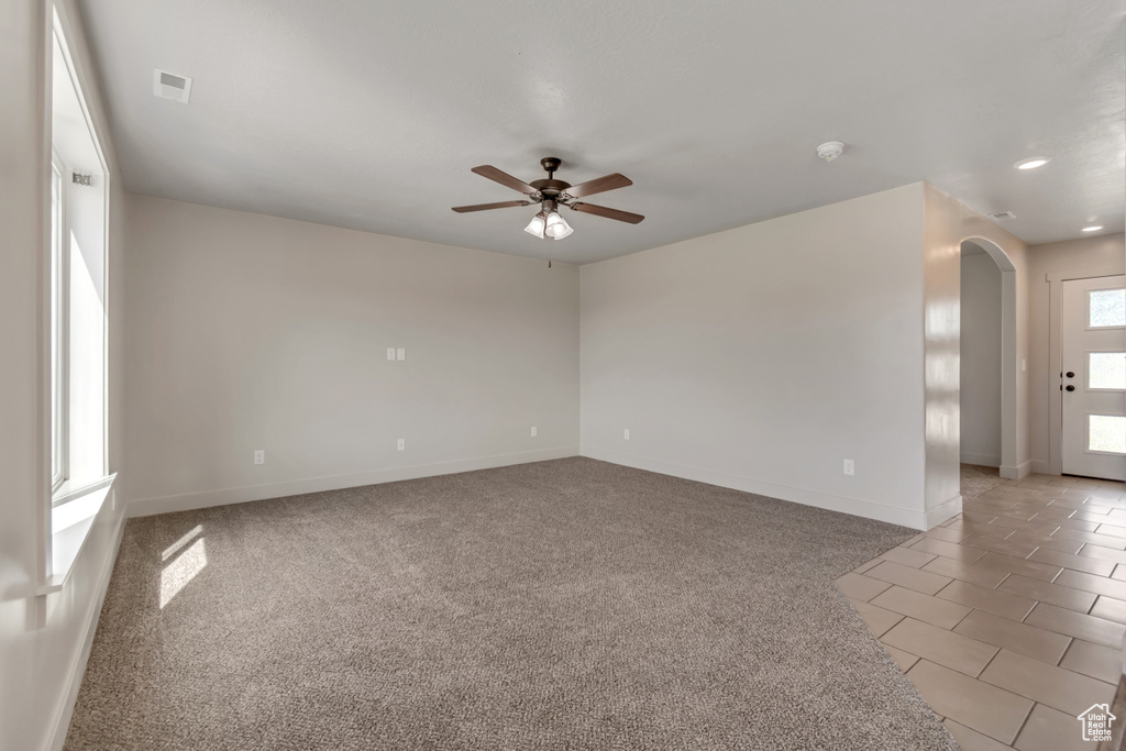 Empty room with arched walkways, ceiling fan, baseboards, and light colored carpet