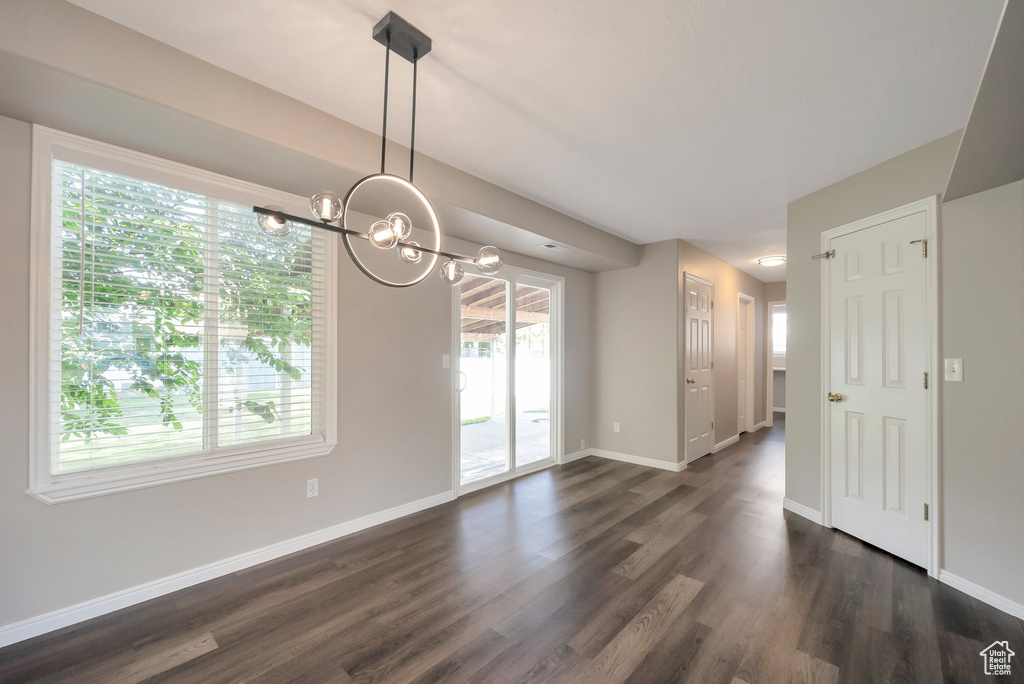 Spare room featuring plenty of natural light, dark wood-type flooring, baseboards, and a chandelier