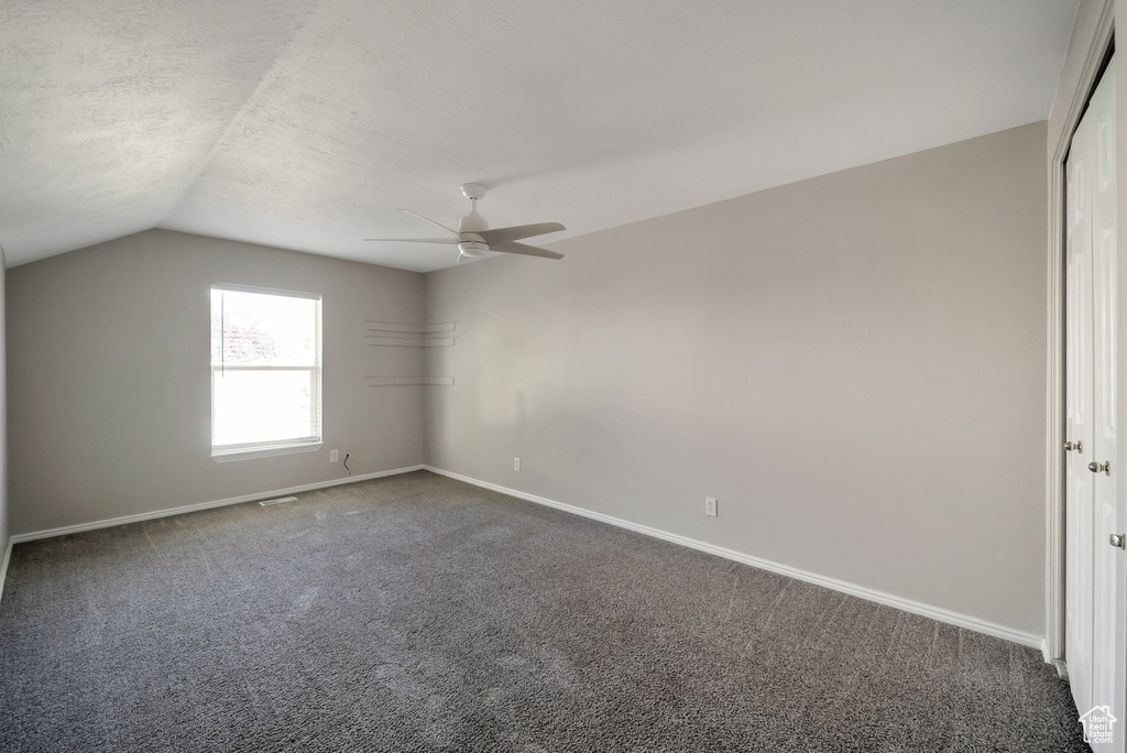 Spare room with dark colored carpet, baseboards, lofted ceiling, ceiling fan, and a textured ceiling