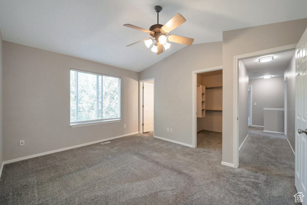 Unfurnished bedroom featuring a walk in closet, lofted ceiling, carpet, baseboards, and a closet
