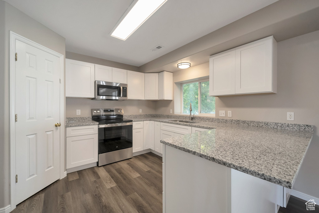 Kitchen with stainless steel appliances, a peninsula, a sink, dark wood-style flooring, and white cabinetry