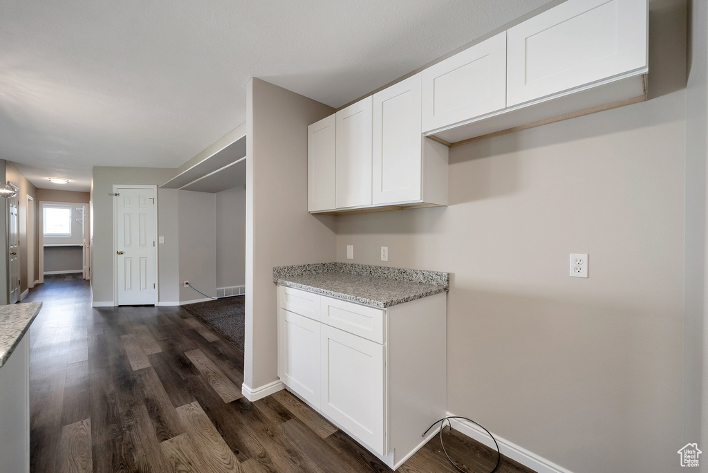 Kitchen featuring dark wood-style flooring, light stone countertops, white cabinets, and baseboards