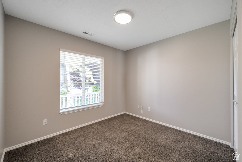 Spare room featuring dark colored carpet and baseboards