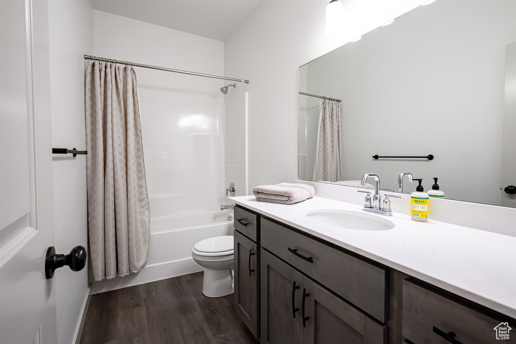 Bathroom featuring wood finished floors, vanity, shower / bath combo with shower curtain, and toilet